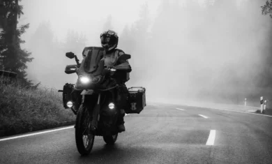 Adventure motorcycle rider in full gear navigating a foggy forest road in black and white.