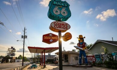 a statue of a cowboy holding a surfboard in front of a gas station