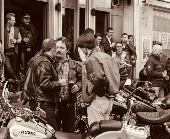 Home Motorcyclists in leather gather outside a city cafe, sharing conversations and camaraderie.