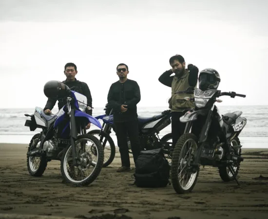 Home Three men with motorcycles enjoying a beach ride, showcasing freedom and adventure.