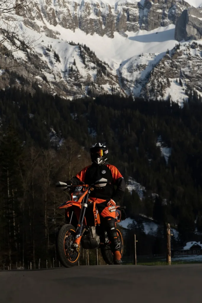 Motorcycle Riding Boots man in orange and black jacket riding orange motocross dirt bike on snow covered mountain during